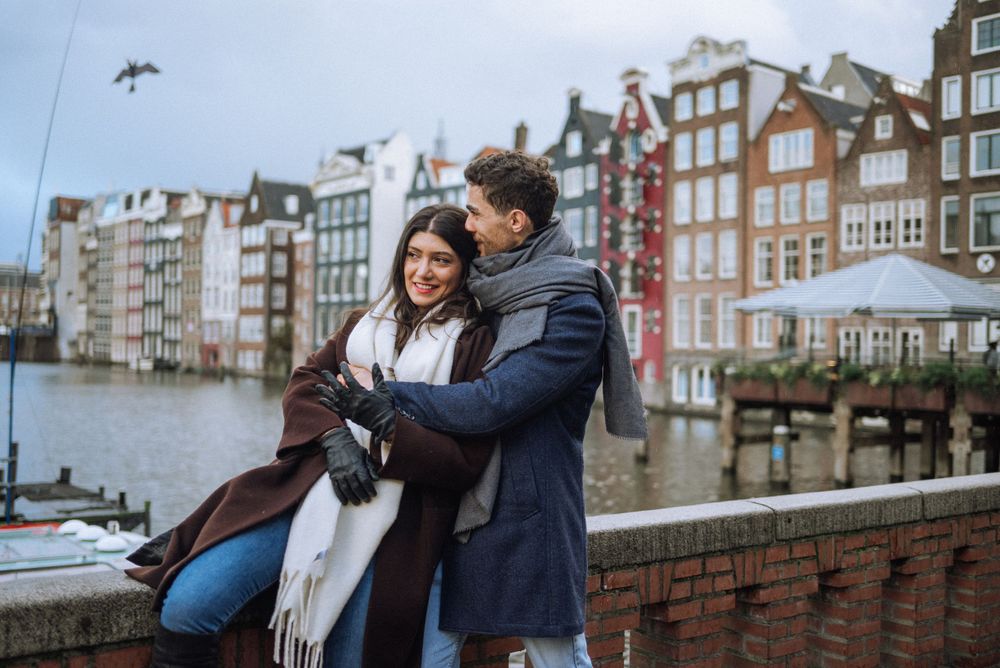 Couple embracing on Amsterdam canal with traditional Dutch houses in background.