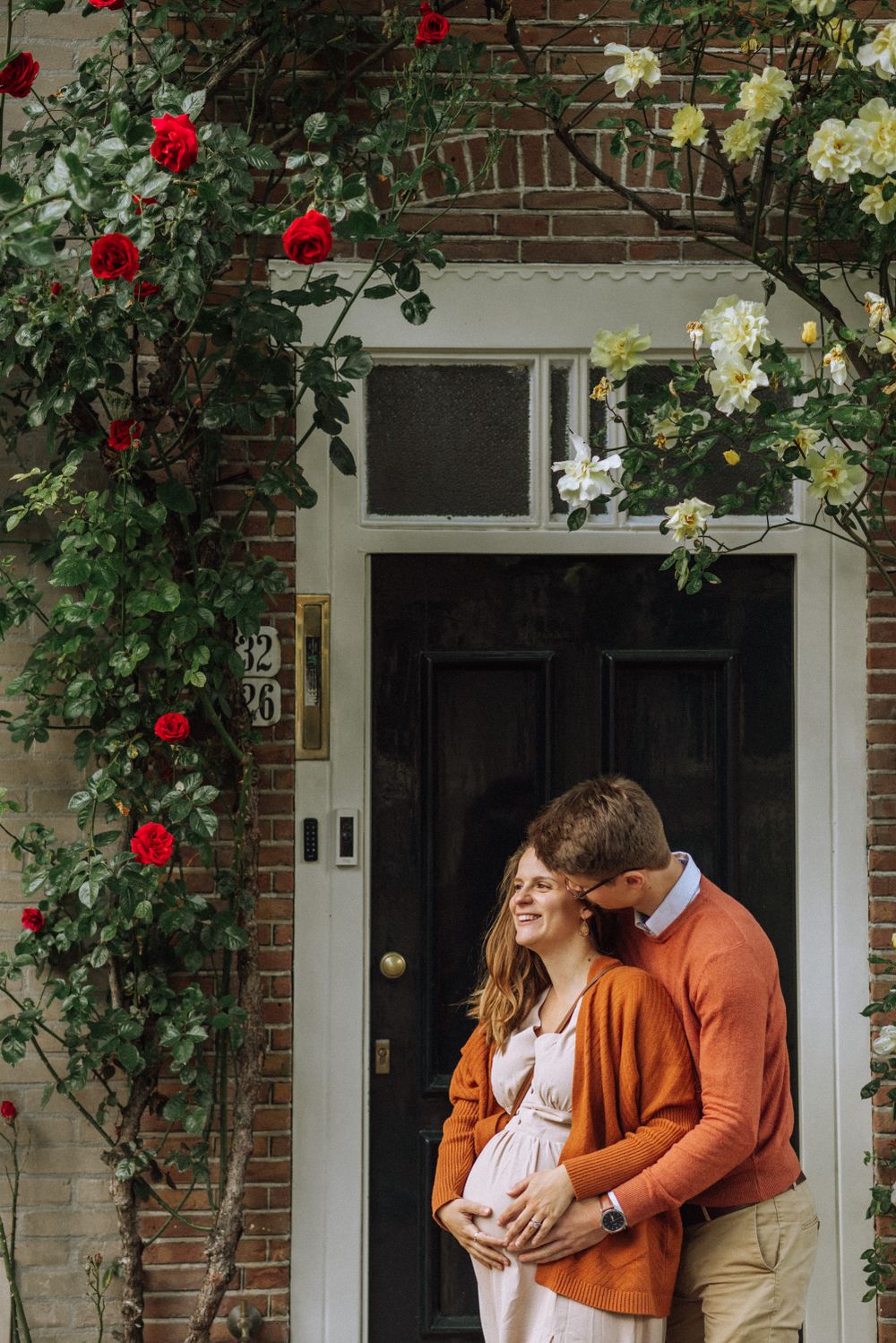 Couple embraces by doorway framed with climbing red and white roses.