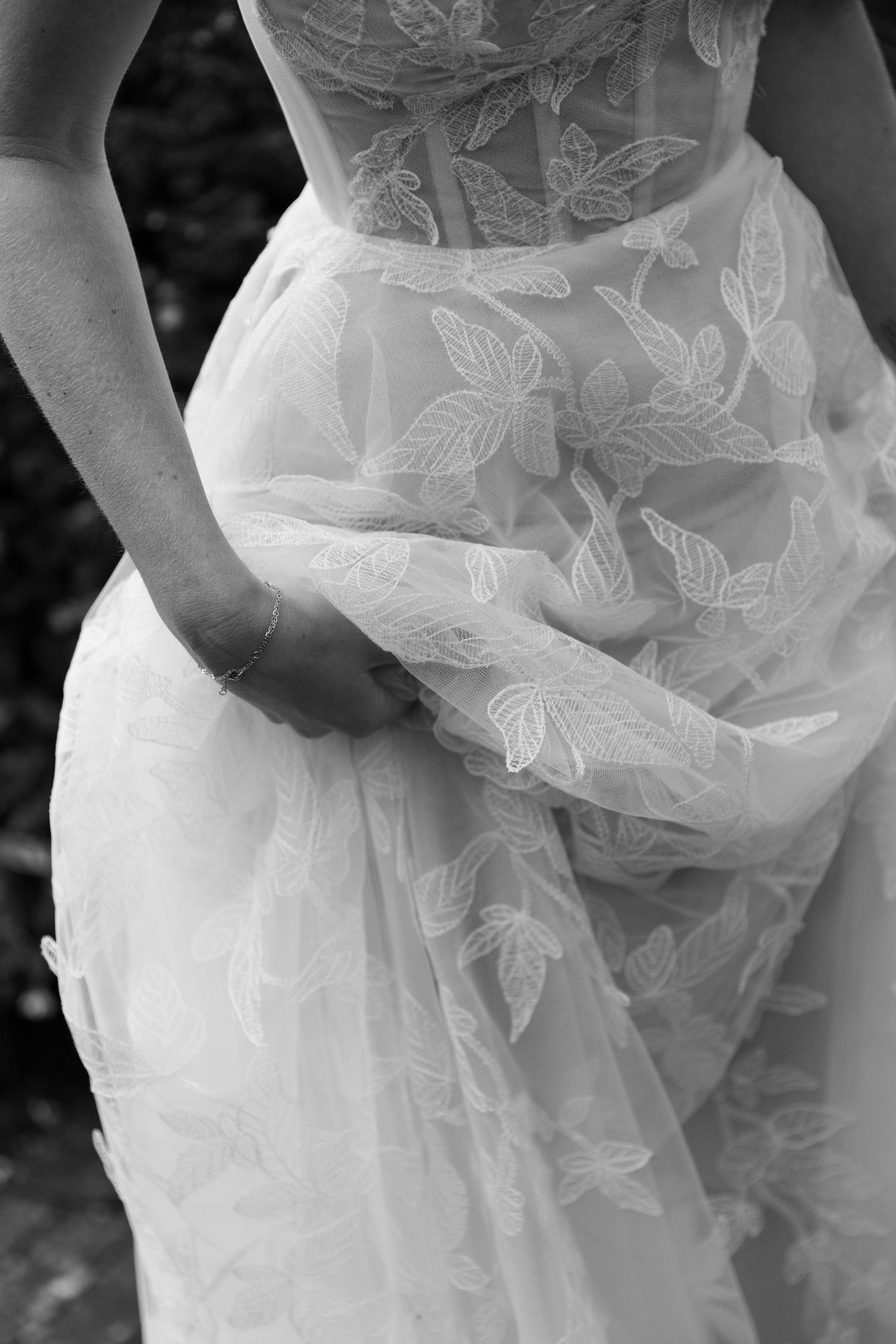 Close-up black and white detail of a delicate wedding gown with embroidered leaf patterns and sheer overlay fabric.