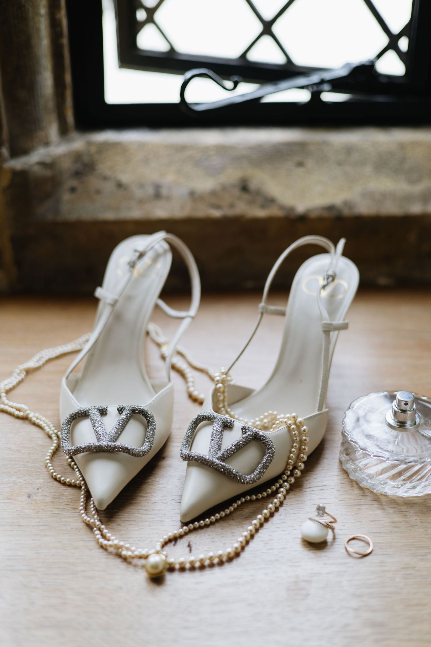 Elegant bridal shoes with crystal embellishments and pearl jewelry on windowsill.