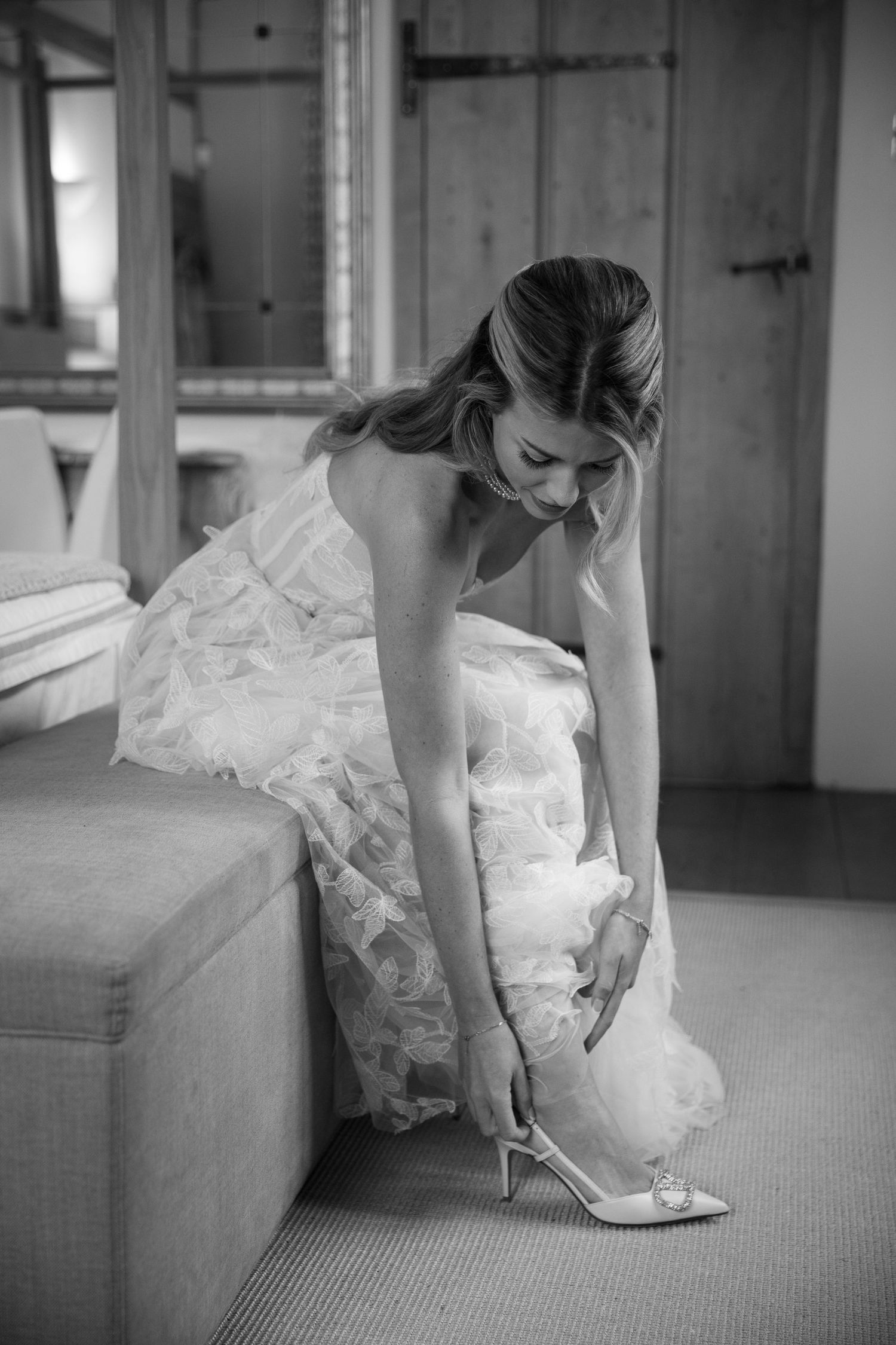 Black and white photo of bride putting on sparkly wedding shoes.