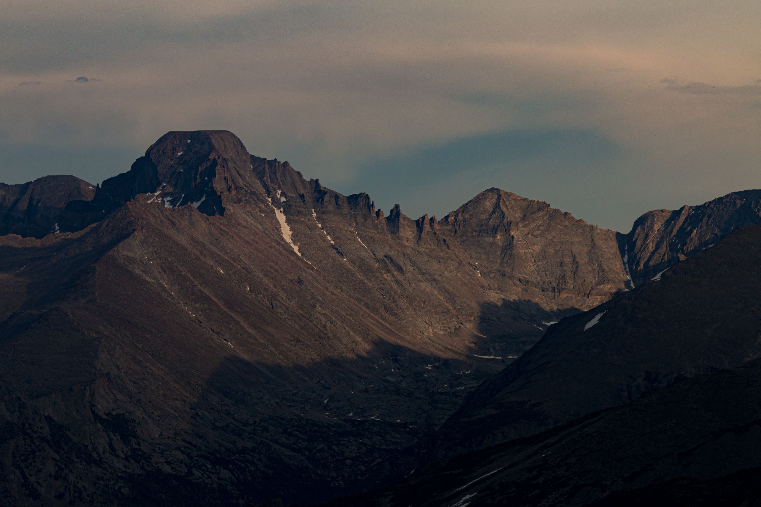 Rugged mountain peaks cast in shadow during golden hour with dramatic cloud formations above.