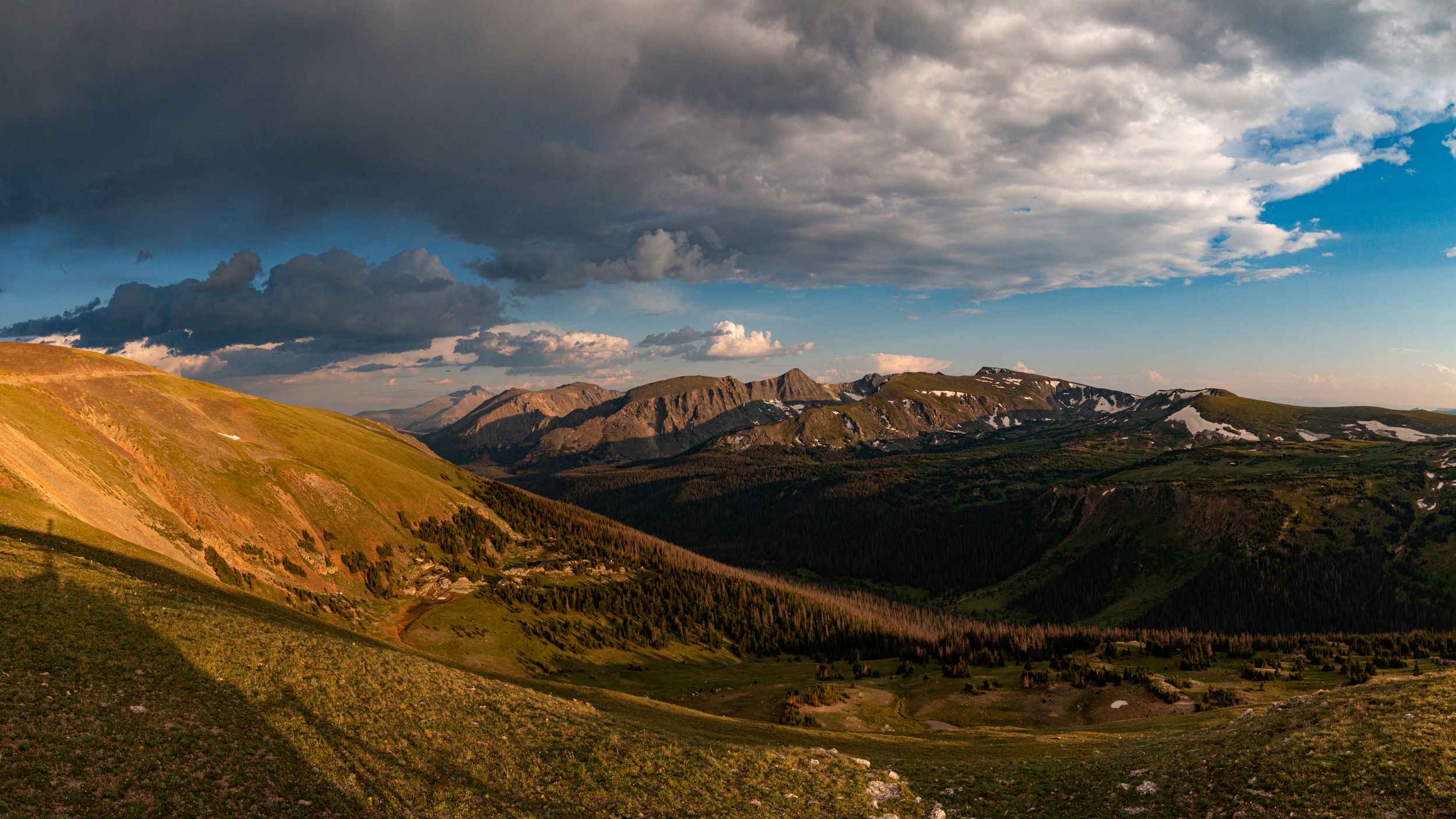 Scenic mountain landscape with golden hillsides and dramatic storm clouds rolling over distant peaks.
