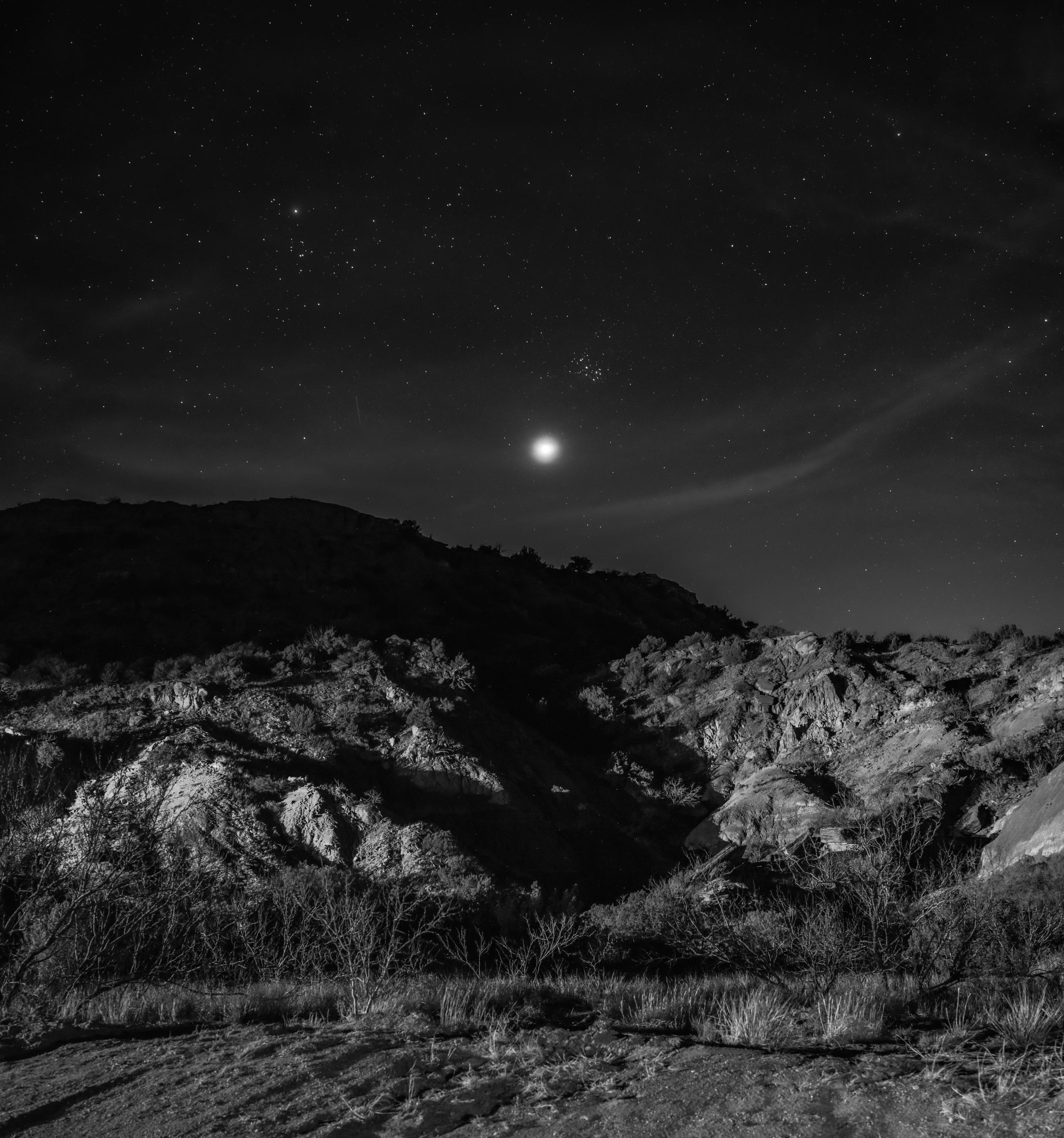 Moonlit mountain landscape in black and white with rocky terrain and dramatic shadows.