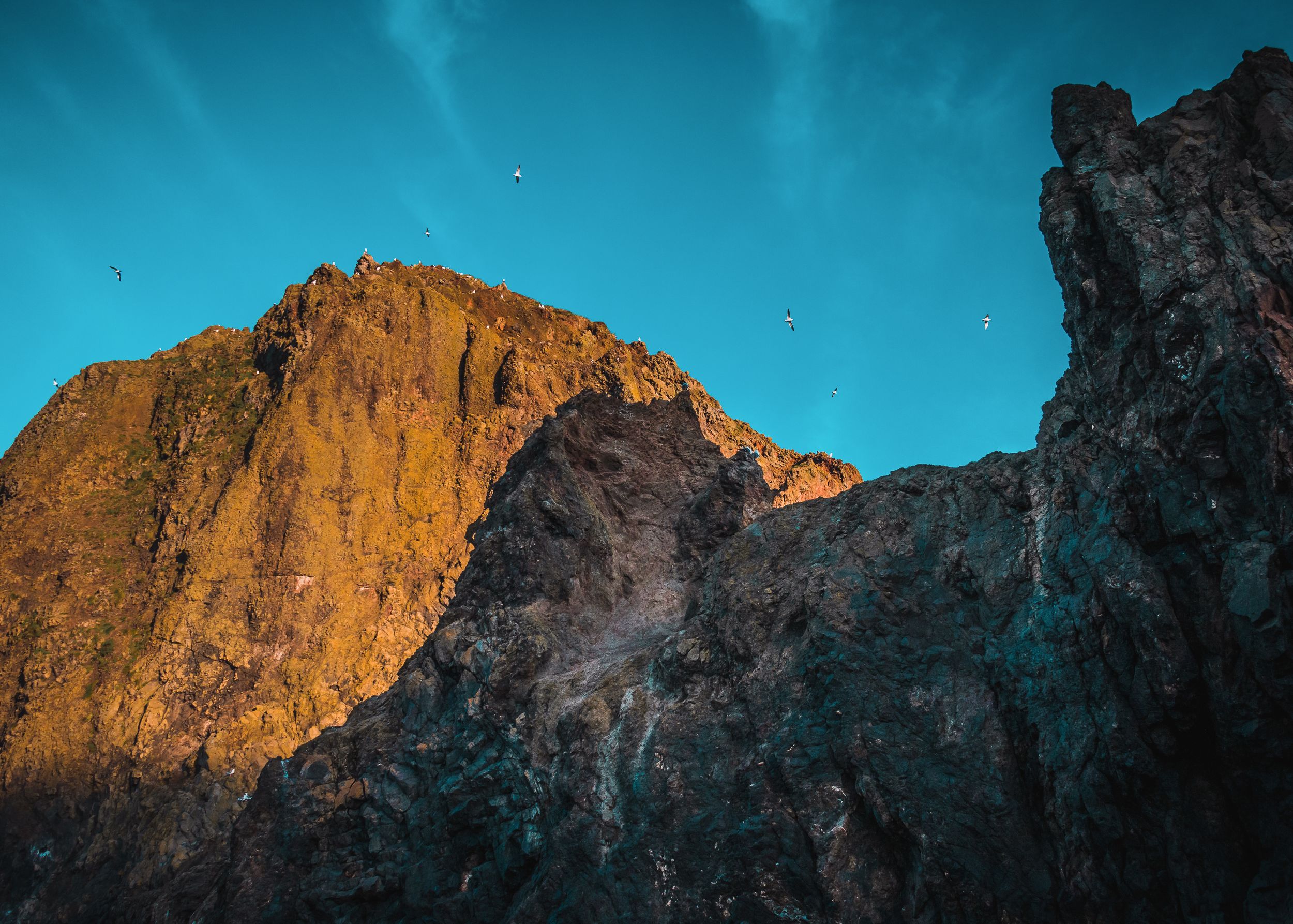 Majestic rocky mountain peak glows orange in sunlight against vibrant turquoise sky.