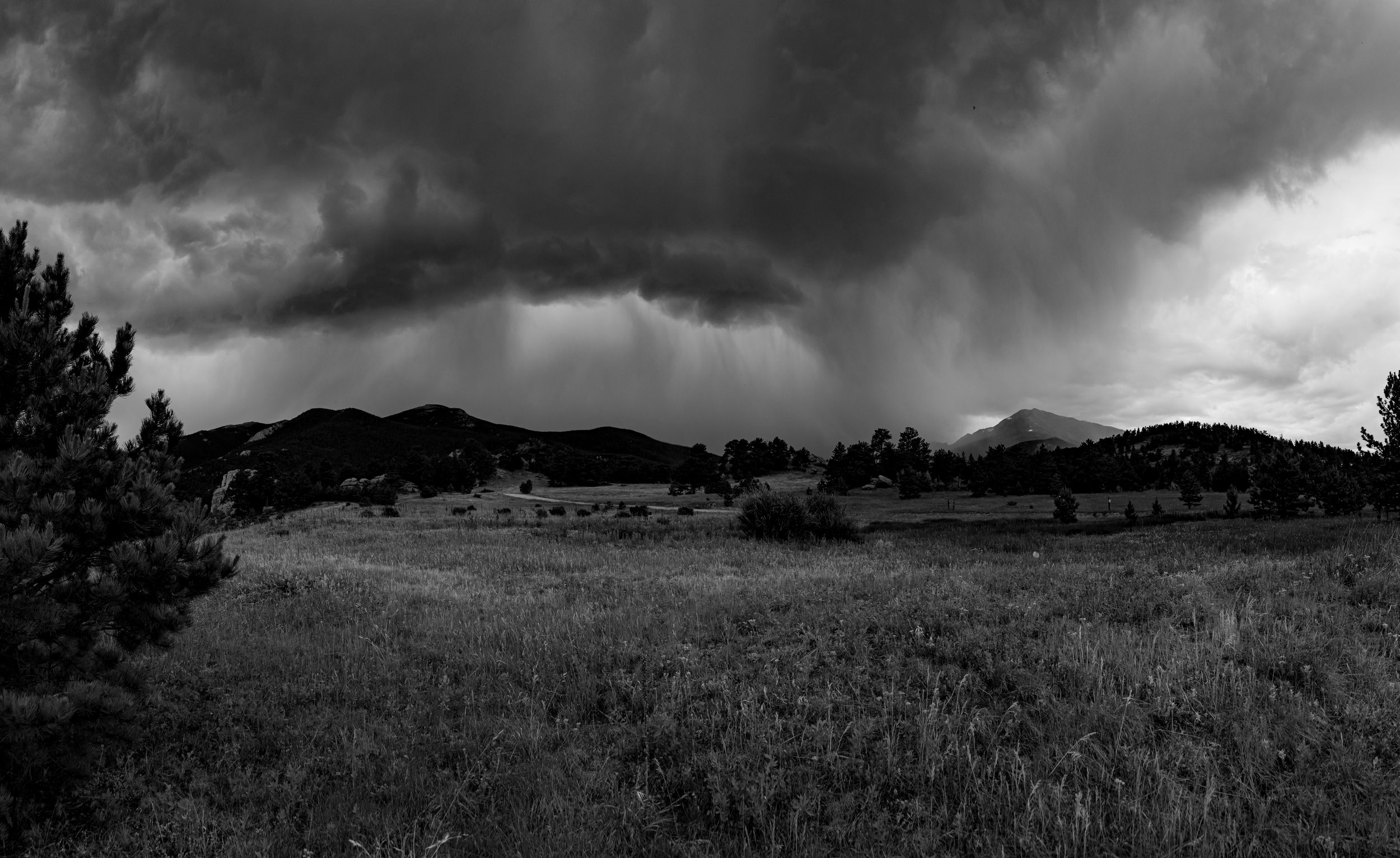Dramatic storm clouds gather over a mountain landscape in black and white, creating an ominous atmosphere.