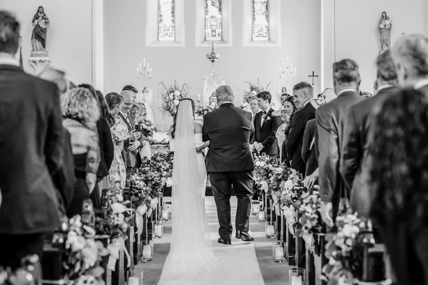 Black and white photo of a church wedding ceremony. Bride walking down the aisle at a Leitrim church wedding. emotional groom reaction.
