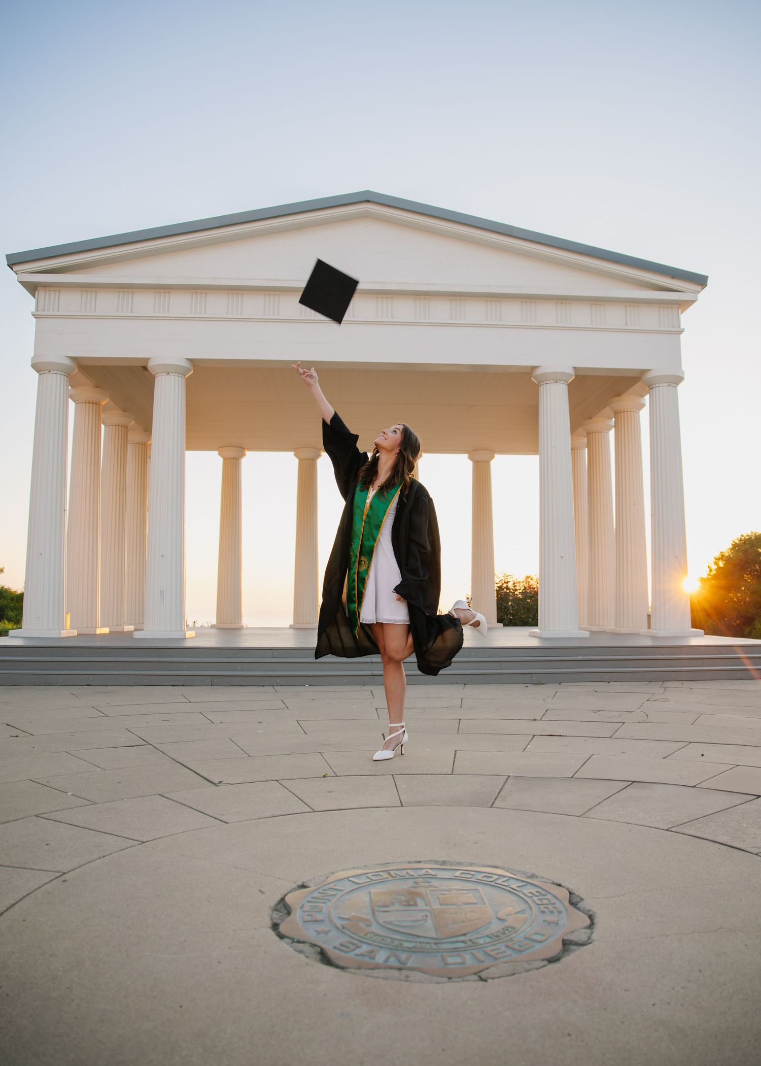 Graduate in cap and gown posing for portraits on wooden steps with bright smiles.