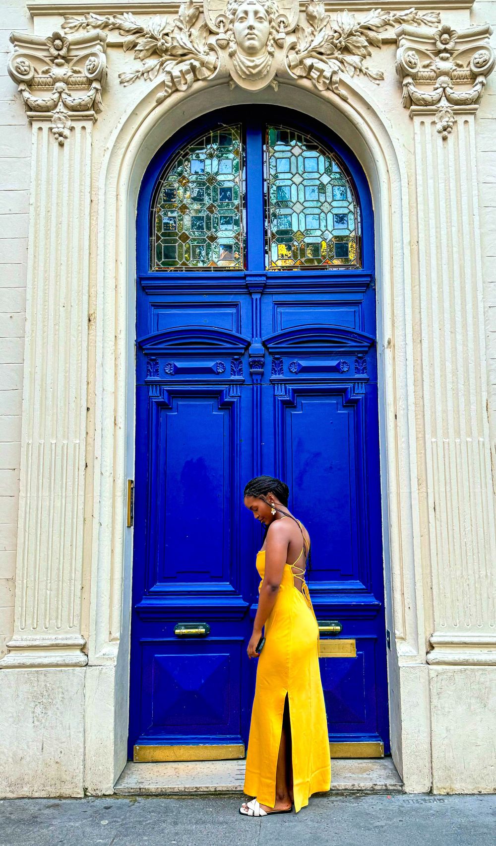 Person in yellow dress poses against ornate blue door with decorative white stone archway.
