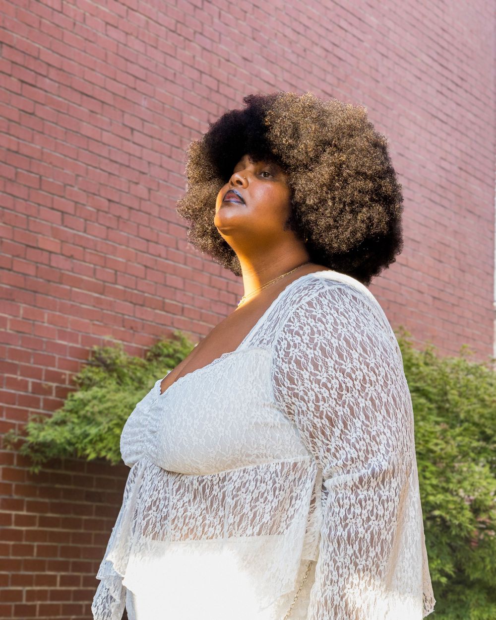 Artistic fashion portrait against red brick wall featuring white lace dress in natural light.