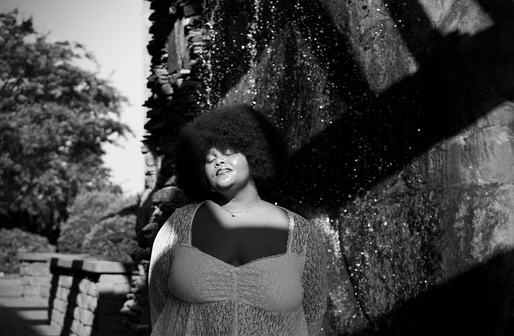 Dramatic black and white fashion portrait with natural lighting and architectural elements.