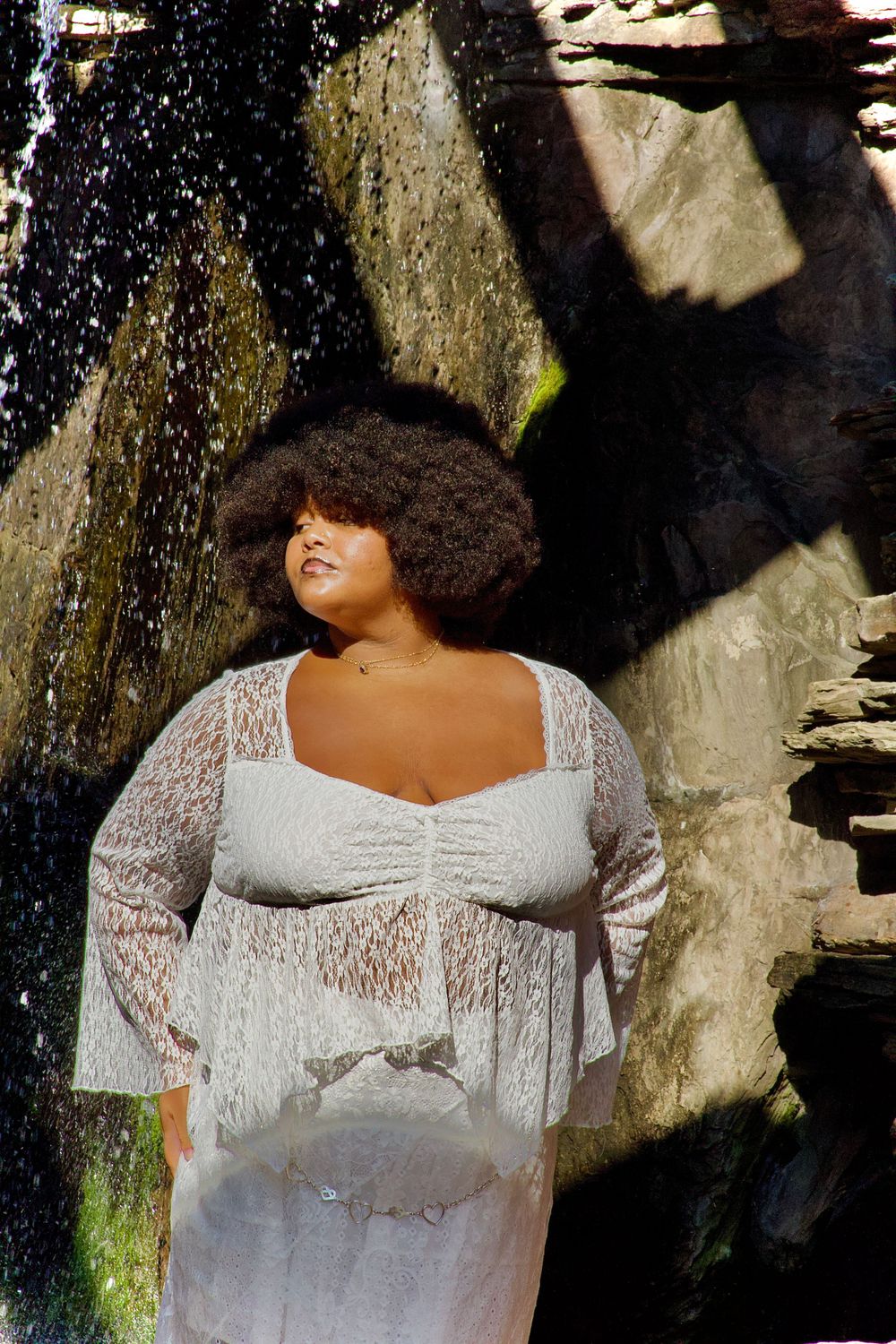 A white lace dress photographed against a stone wall with cascading water in the background.