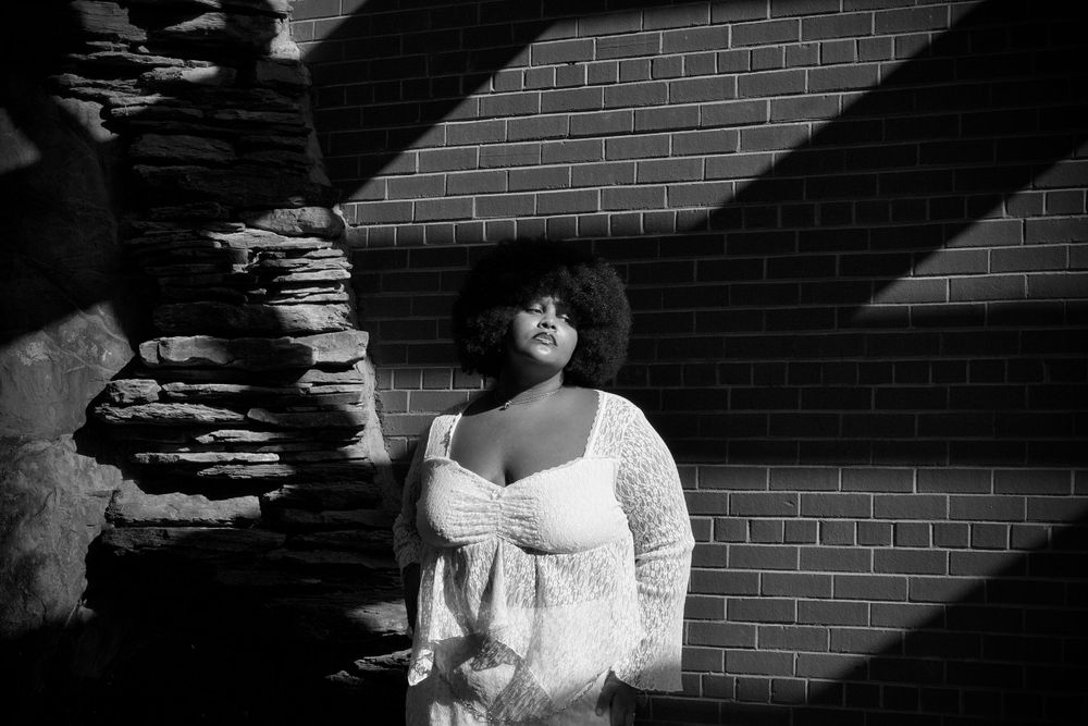 An artistic black and white portrait against a brick wall with dramatic shadows.