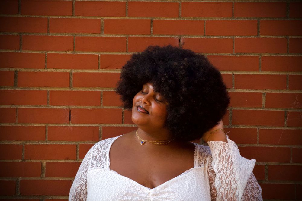 Artistic portrait against brick wall showcasing natural hair and white lace fashion.