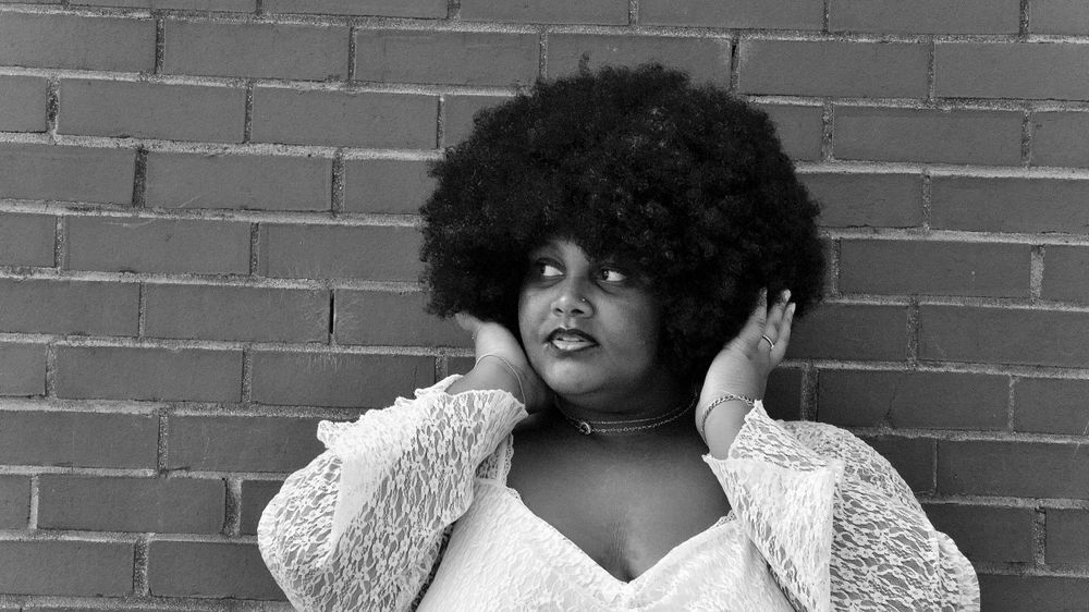 Black and white portrait against brick wall featuring natural hair and elegant style.
