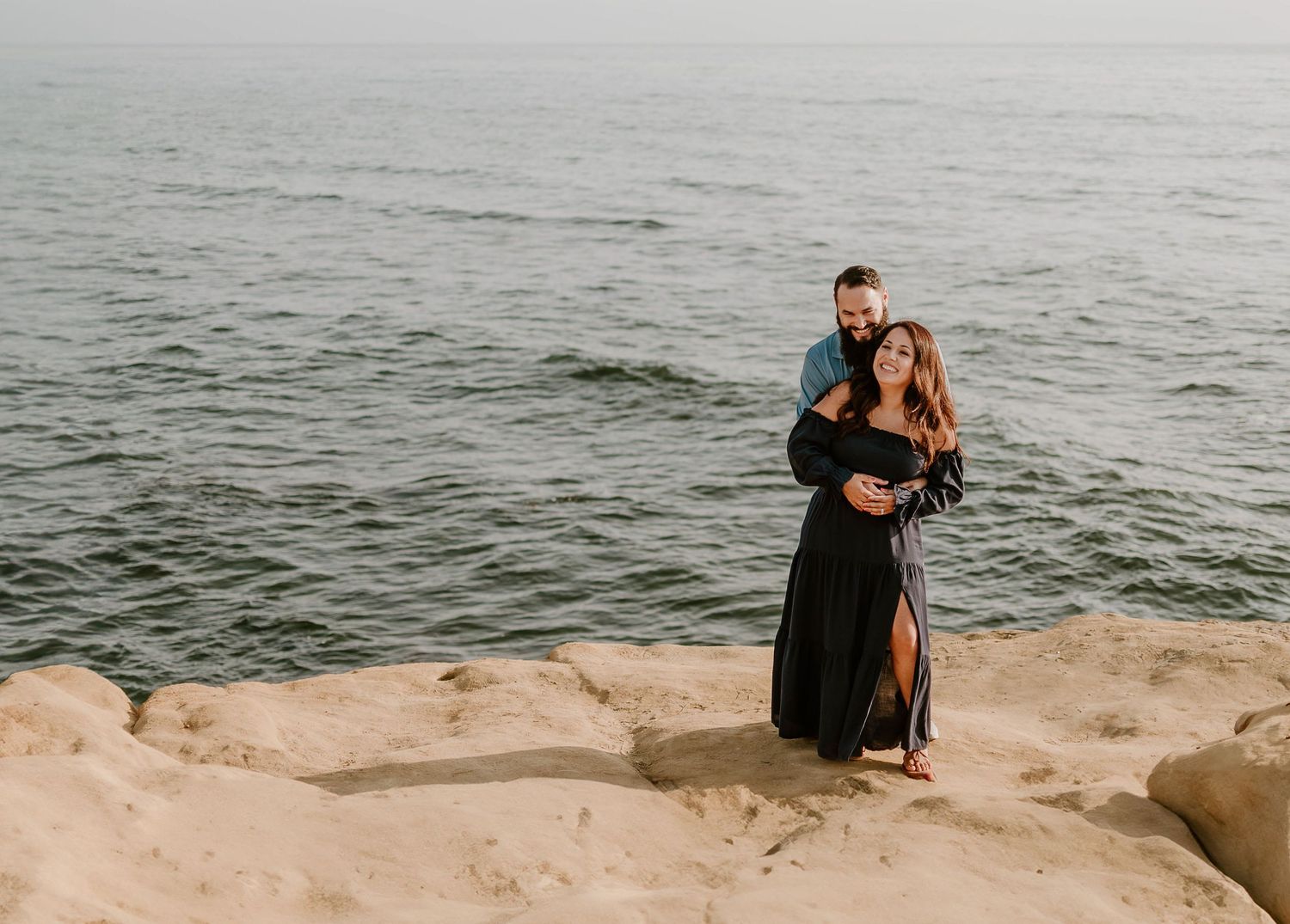 Romantic coastal photoshoot on rocky cliffs overlooking ocean at sunset.