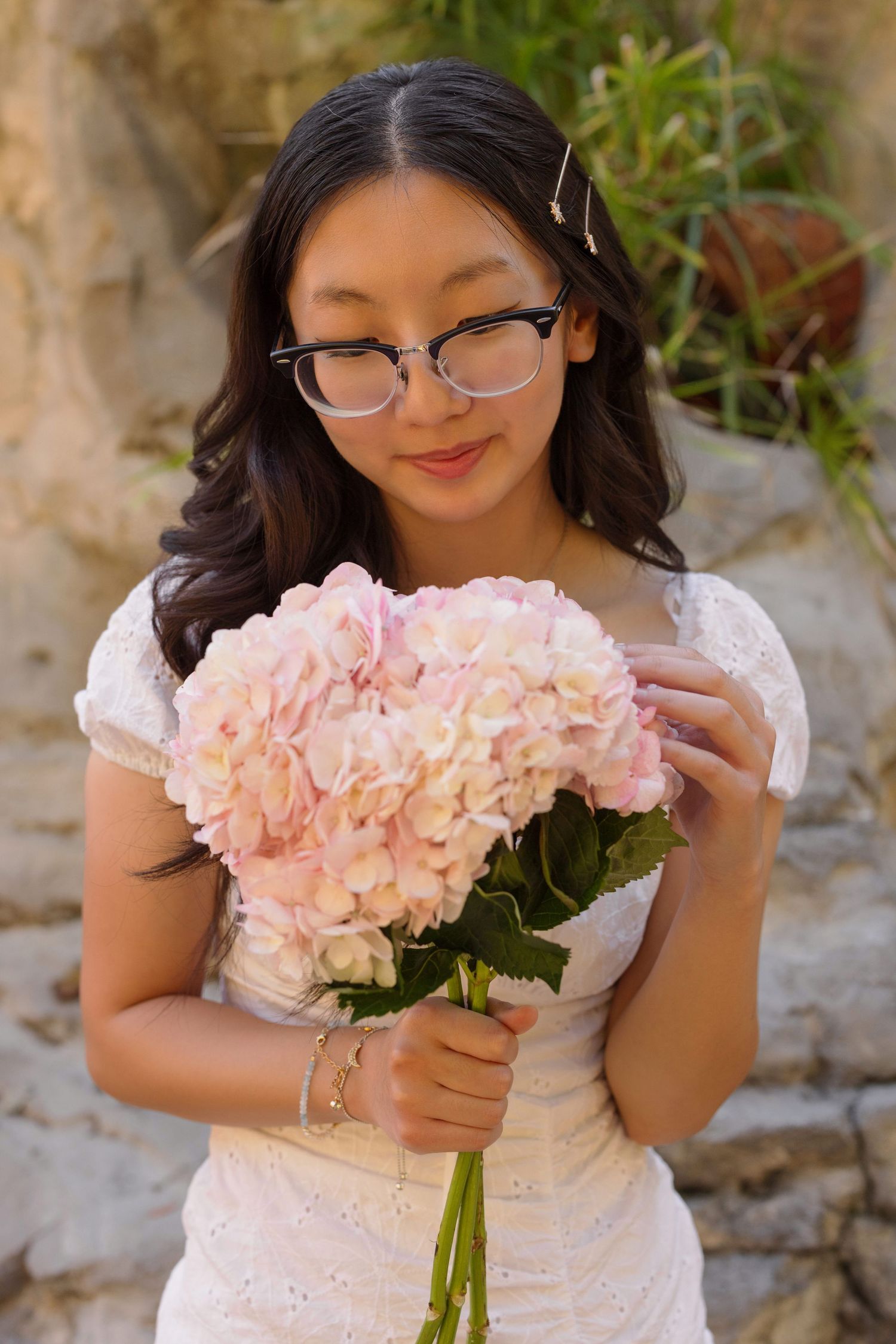 Person holding beautiful pink hydrangea bouquet while wearing white lace dress.