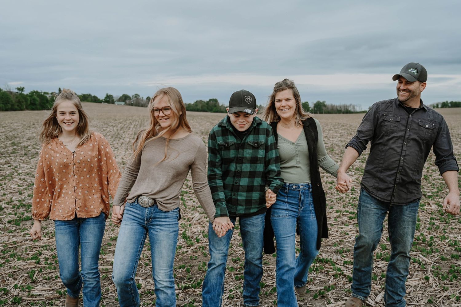 Group of friends stand together on plowed field during overcast day.