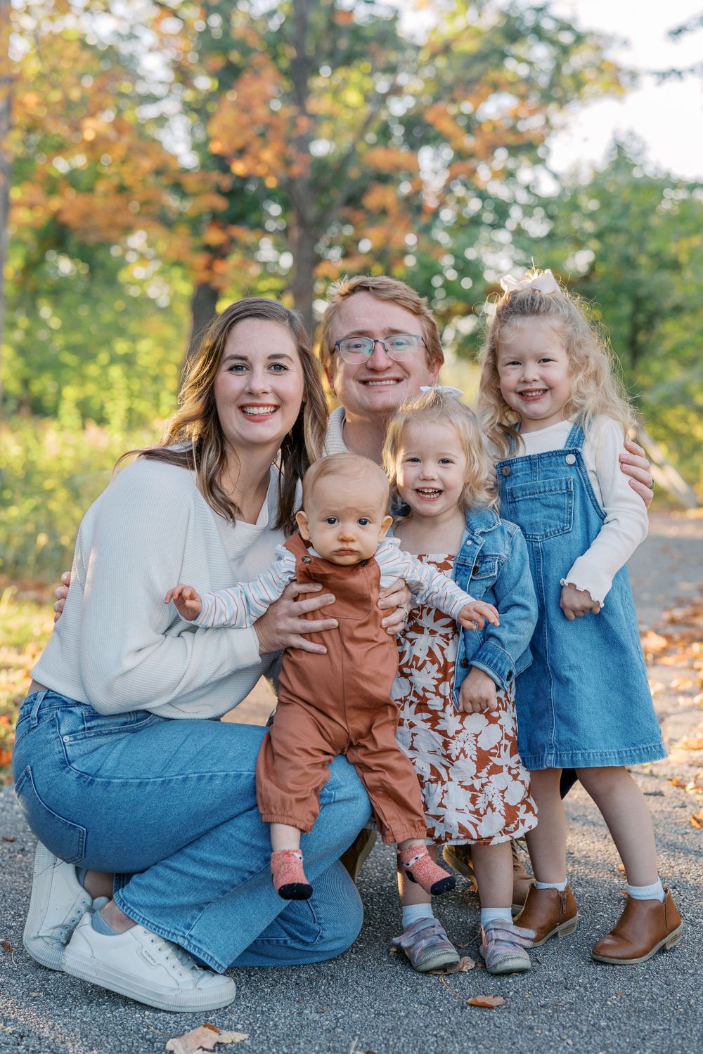 Family sitting together on a path surrounded by fall foliage wearing coordinated casual outfits.