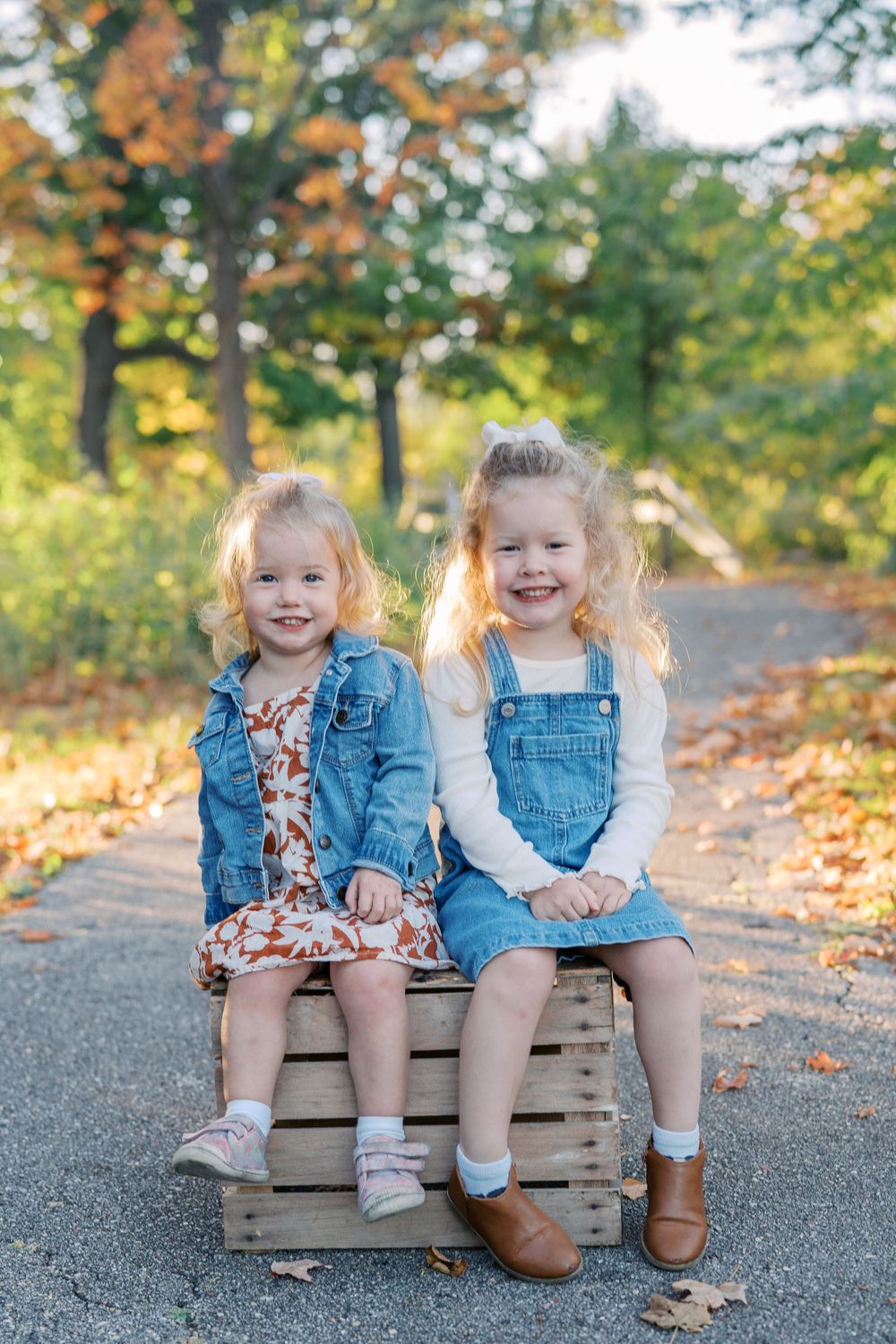 Children in denim outfits sit together on wooden crates during a fall outdoor photoshoot.