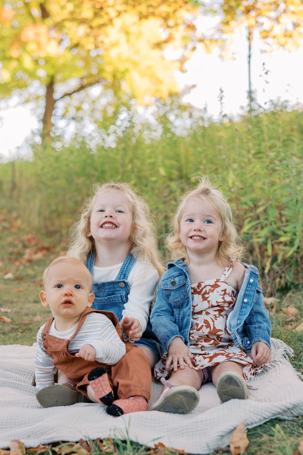 Siblings in coordinated outfits share playful moments on a blanket during an outdoor photoshoot.