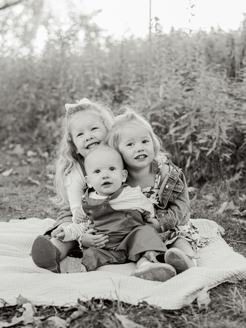 Black and white portrait series of siblings sharing sweet moments on a blanket outdoors.