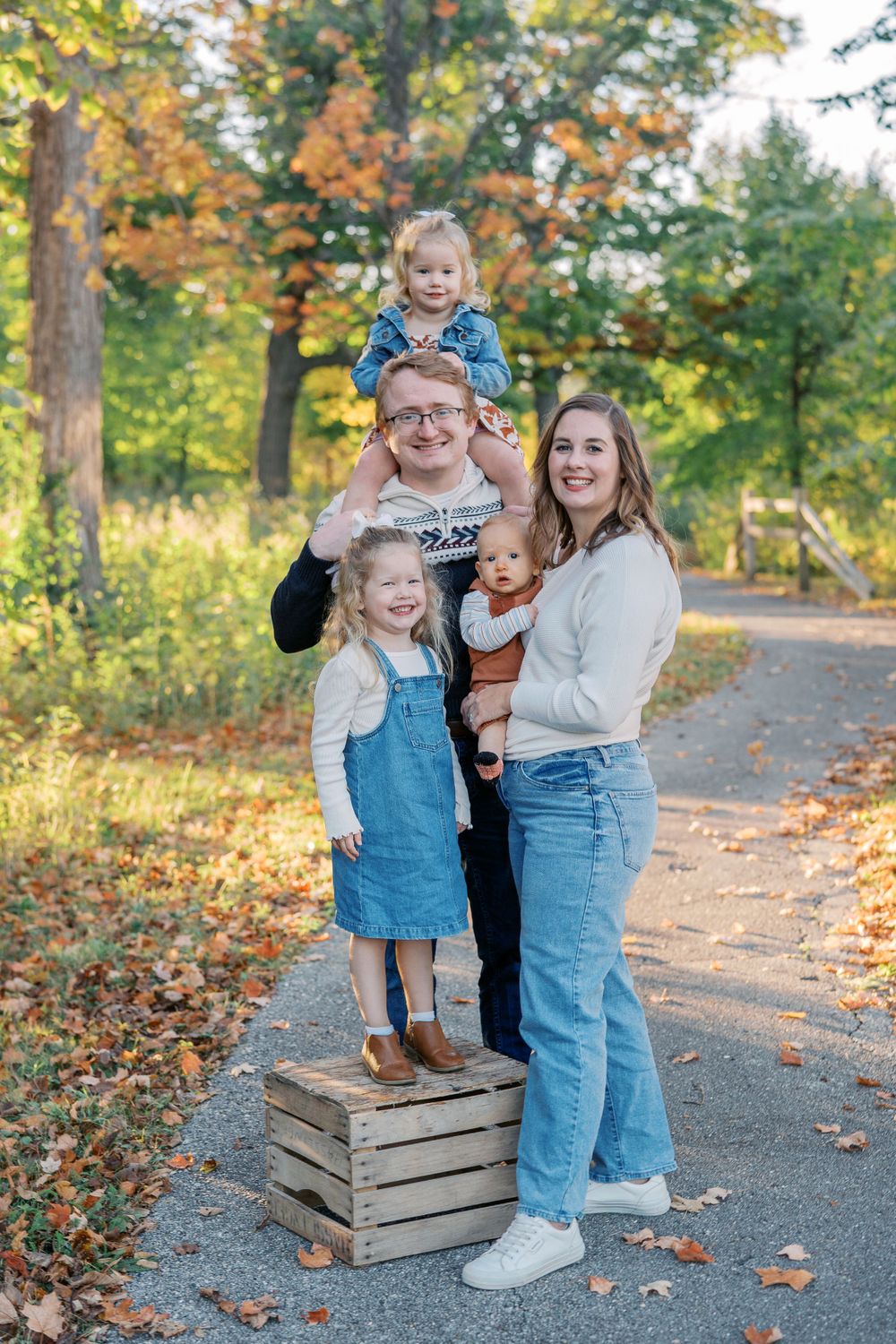 Children in matching denim outfits pose playfully on wooden crates during an autumn photoshoot.