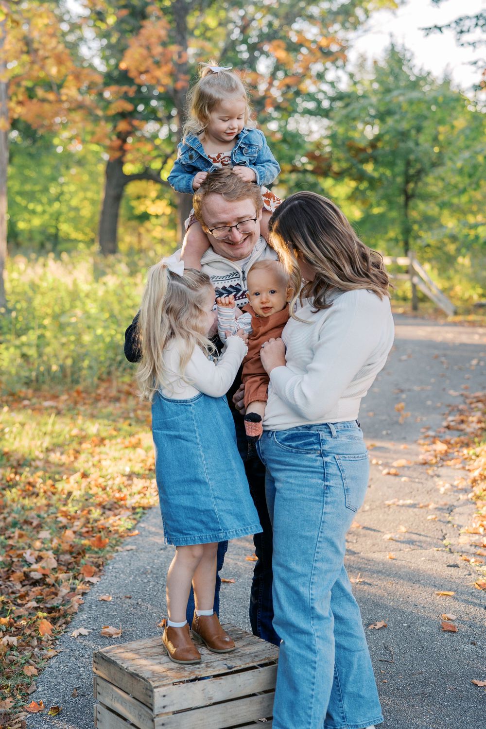 Family gathering on wooden crate for outdoor autumn portrait session.