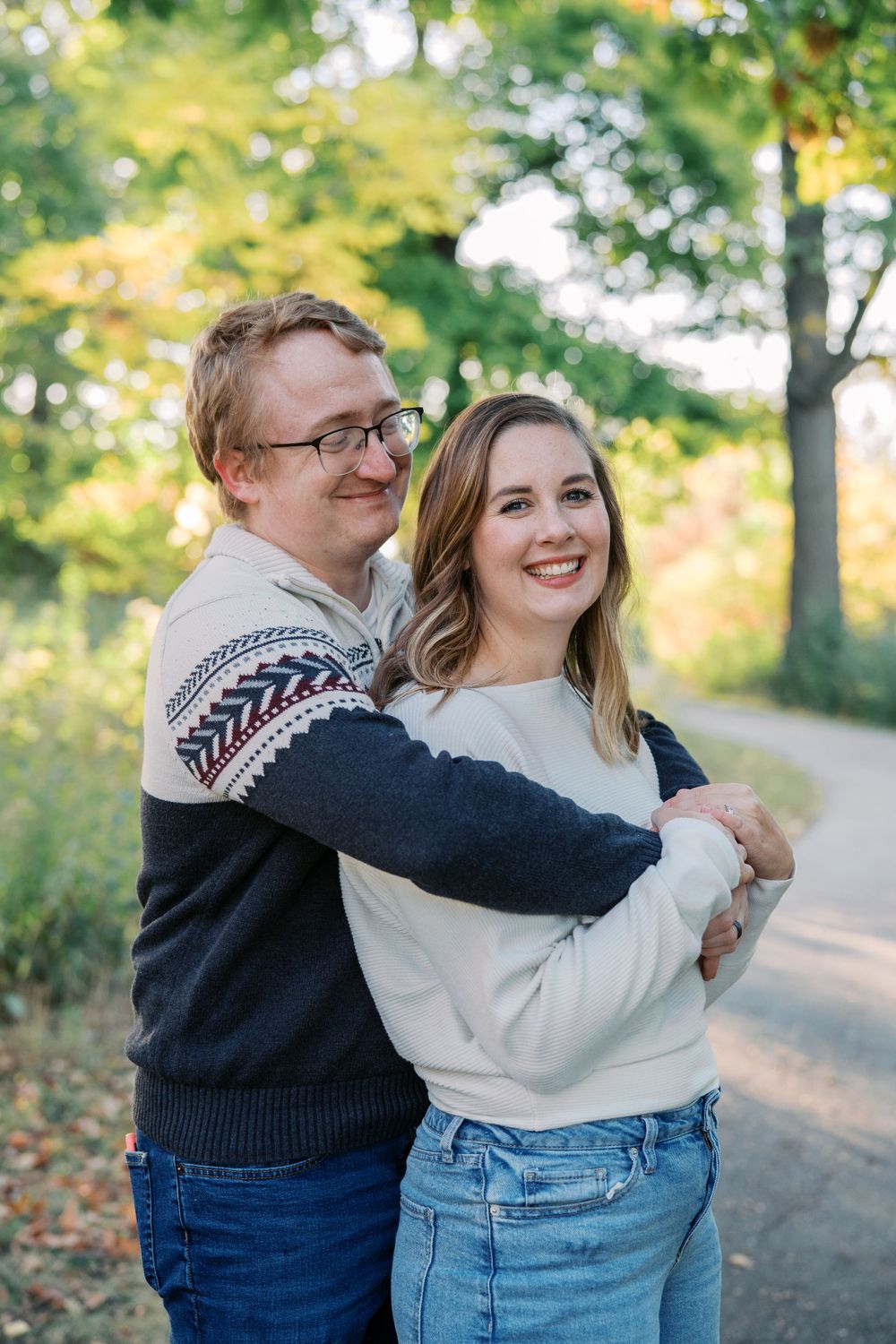 Couple shares joyful embraces during outdoor autumn photoshoot on tree-lined path.