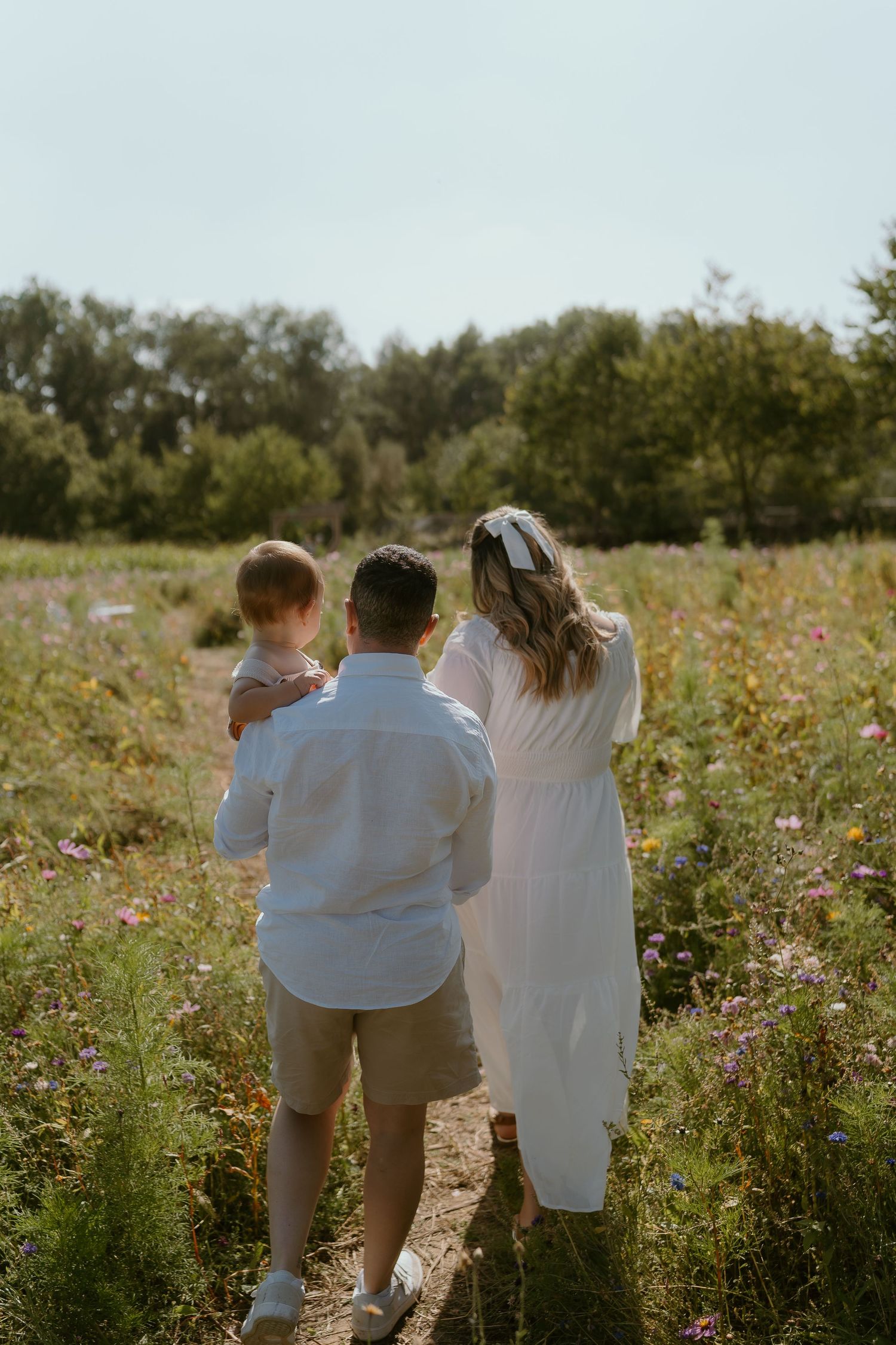 A couple and their child walk through a sunlit wildflower meadow on a summer afternoon in Harrogate.