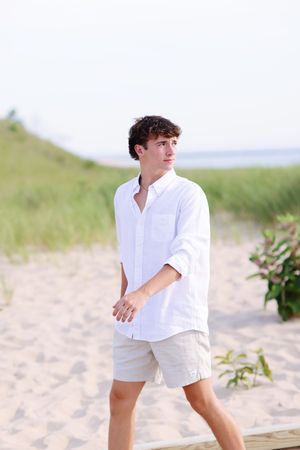 A person in white summer attire walks along a sandy beach on a bright sunny day.