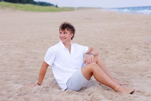 Person in white clothing lounging on sandy beach during summer day.