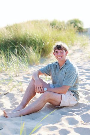 Person relaxing on sandy beach with sea grass in soft natural lighting.