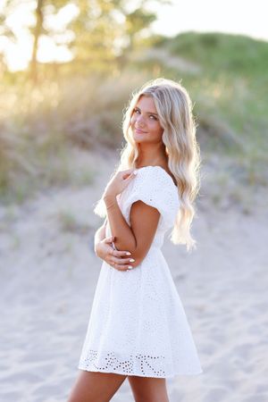 A white eyelet lace dress is worn at the beach during golden hour with sand dunes in the background.