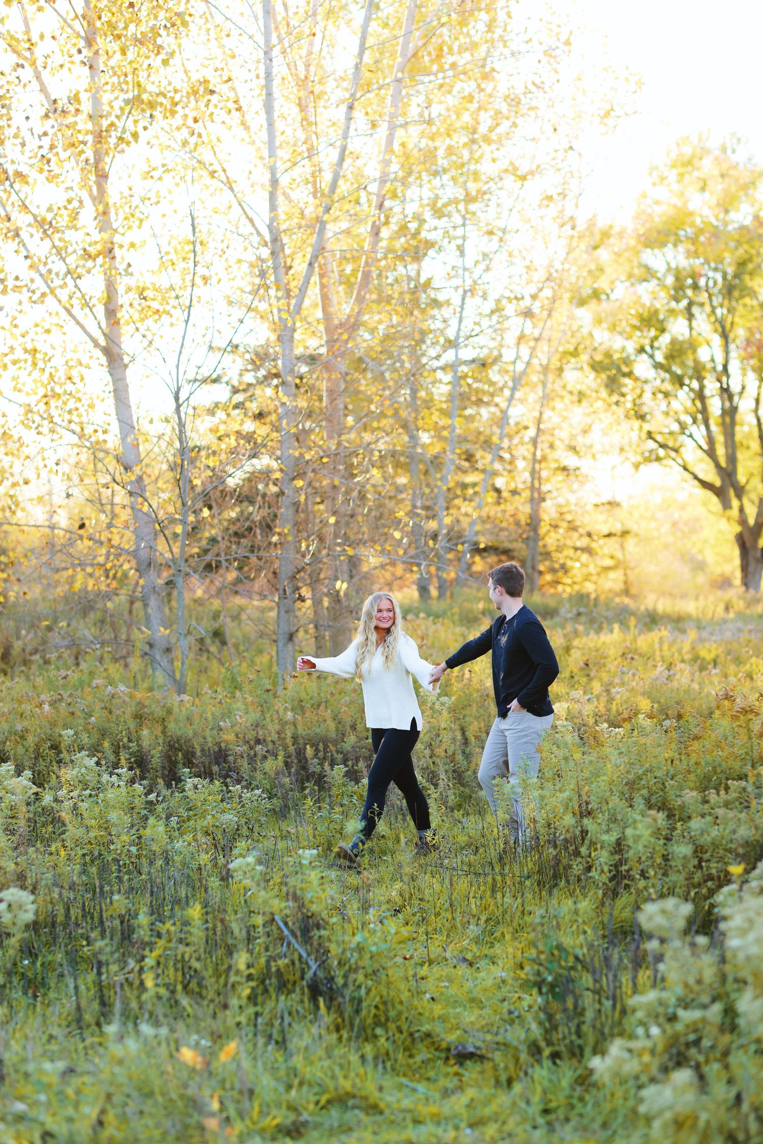 Couple embraces while standing in autumn field during golden hour.