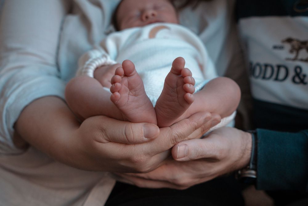 Tiny baby feet being gently held in adult hands against white fabric.
