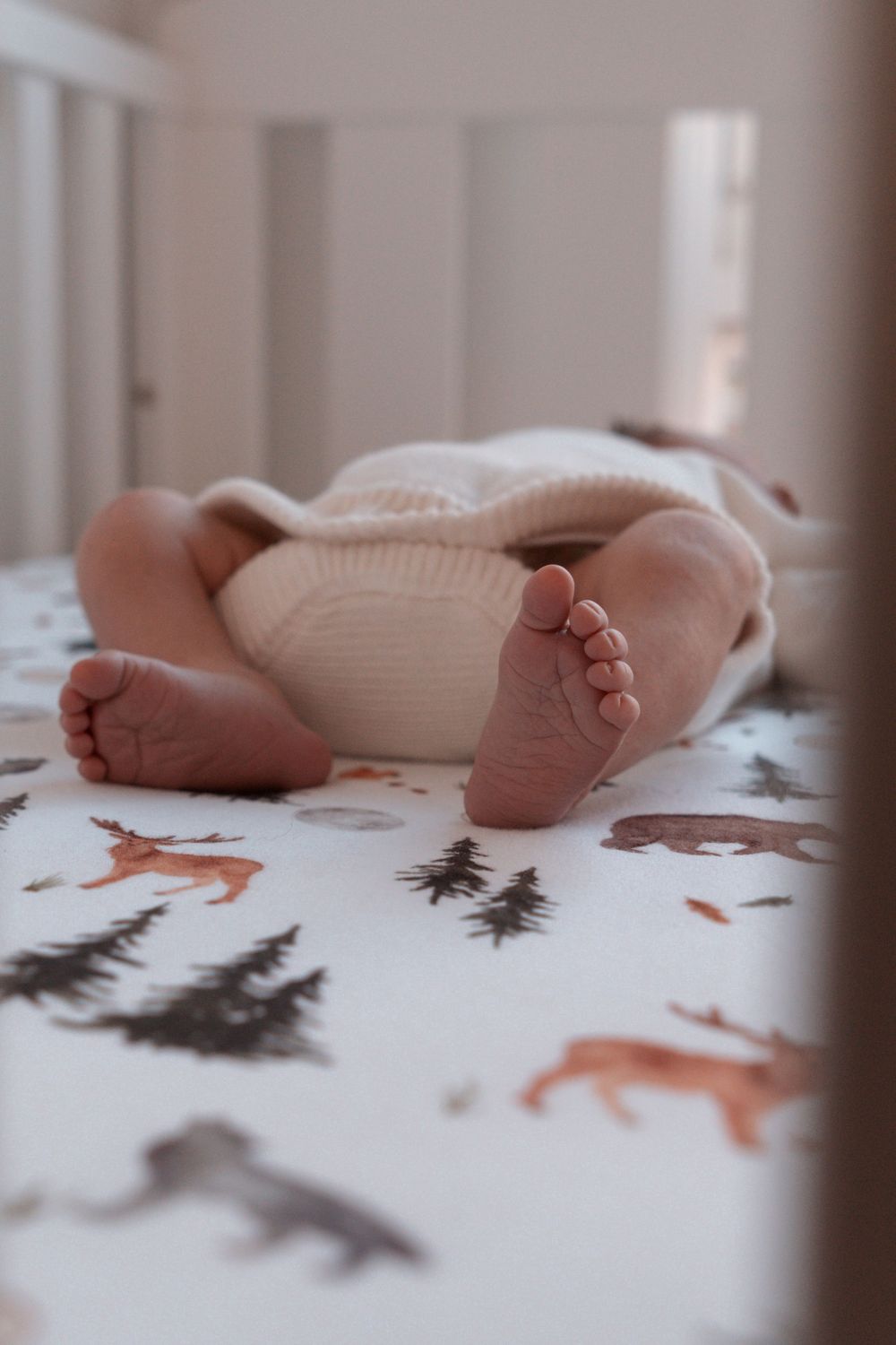 Baby feet resting on woodland-themed cot sheet with fox and tree patterns.