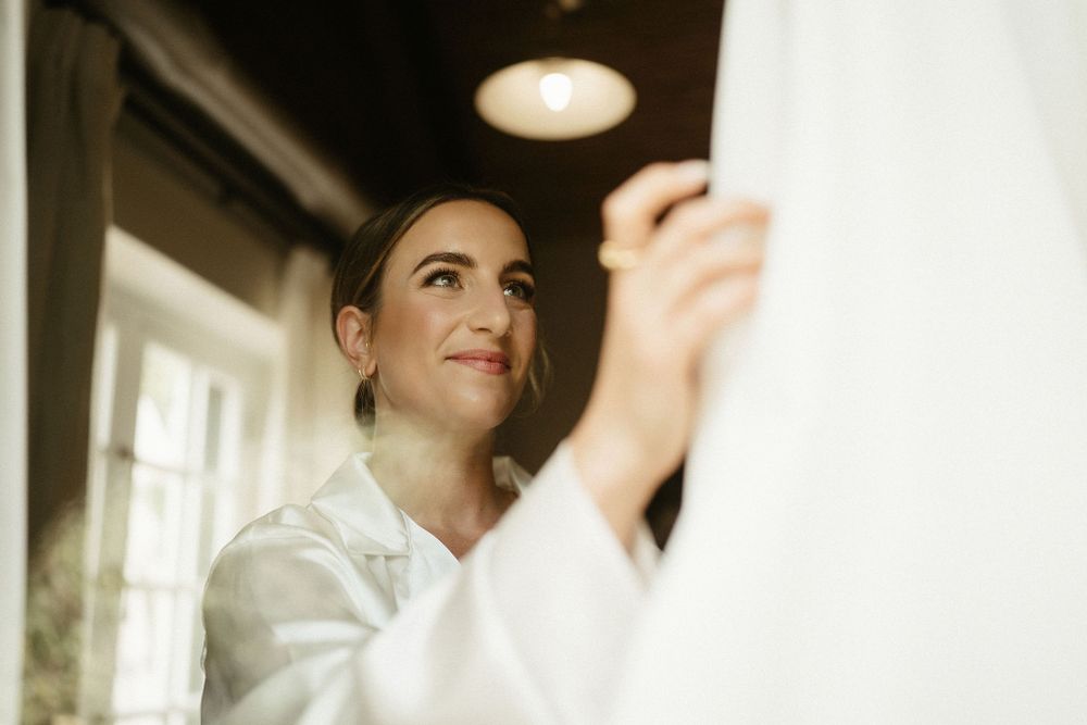 A person wearing a white button-up shirt looks upward with a gentle smile while indoors near a window.