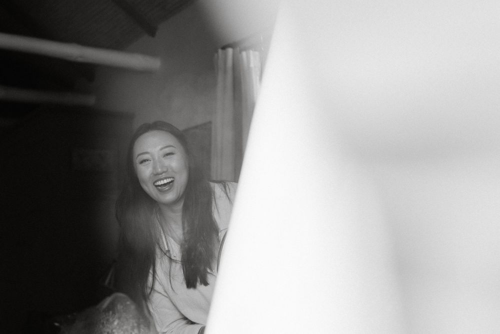 Black and white candid photo showing joyful expression and long hair in dimly lit interior setting.