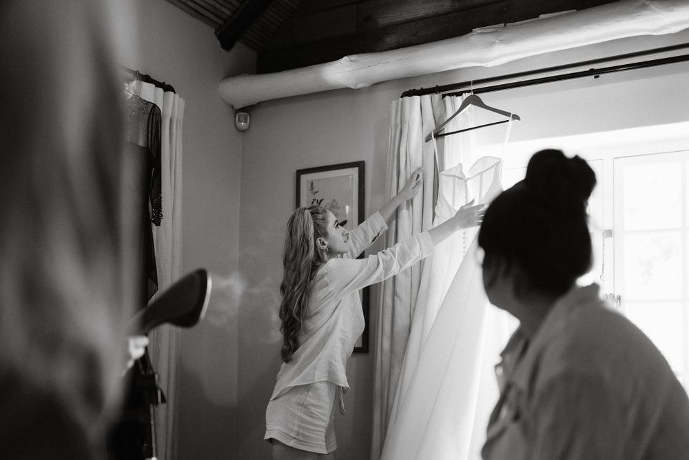 A person in a white shirt reaches up to adjust curtains in a bright interior room with natural light coming through a window.