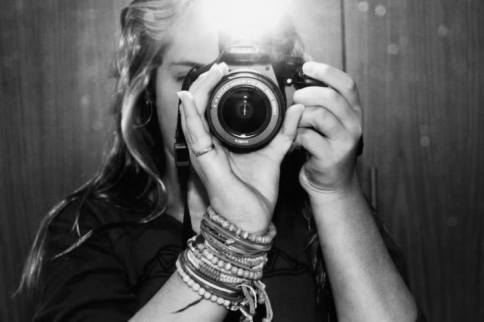A black and white photo of someone taking a photograph with a camera wearing stacked bracelets.