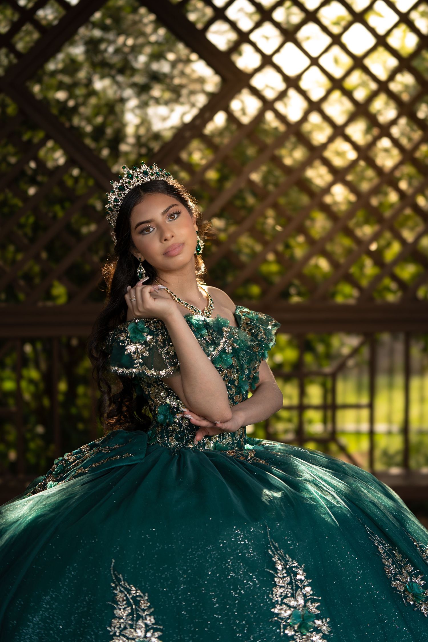 Elegant green ball gown with silver embellishments photographed in garden setting with lattice background.
