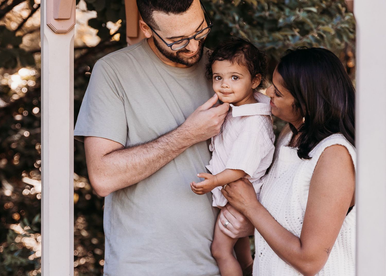 Tender family moment with baby outdoors on a sunny day with natural light filtering through trees.