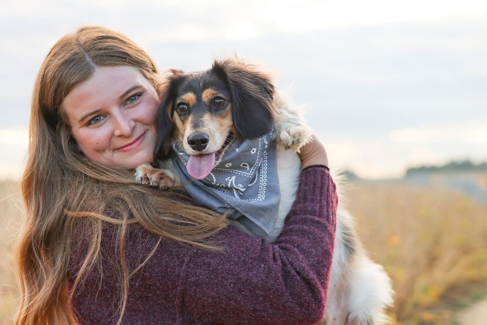 A happy dog wearing a bandana poses outdoors with their human companion at sunset.