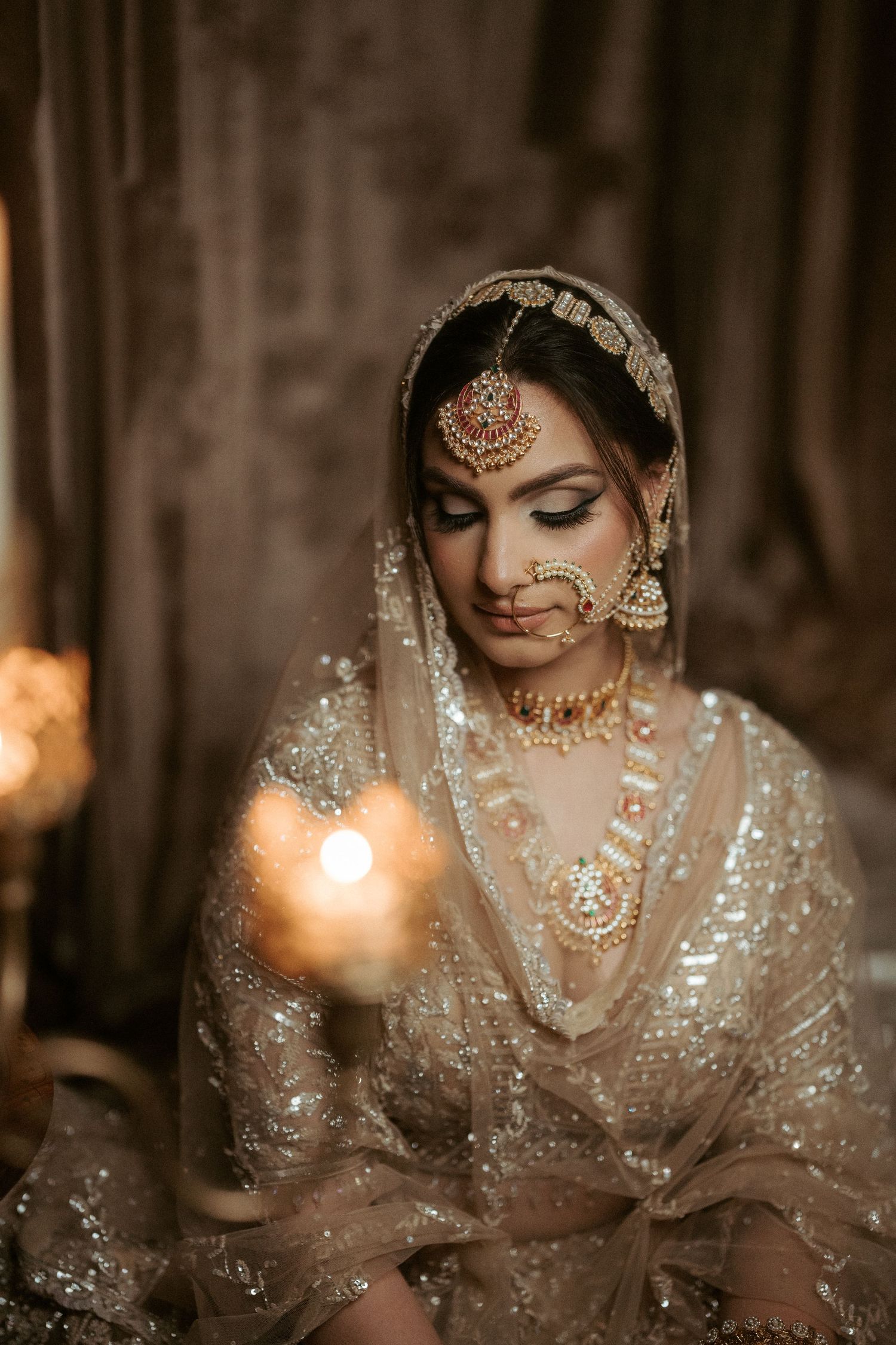 Traditional South Asian bridal portrait with ornate jewelry and intricate henna details in warm lighting.