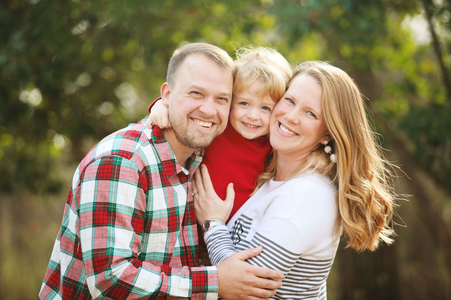 A cheerful family in casual clothing poses outdoors during an autumn photo session.