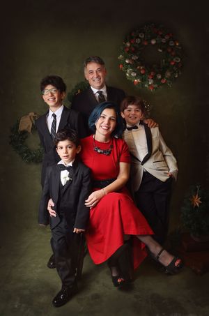 Family wearing formal attire poses together against dark backdrop with red holiday wreath decorations.