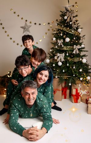 Family in matching green holiday pajamas lies on floor by Christmas tree with gold star decorations.