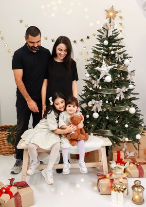 A family poses for a series of holiday photos in matching black and white outfits next to a decorated Christmas tree.