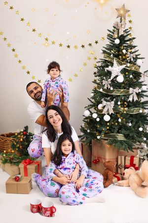 A family wearing matching Christmas pajamas poses together in front of a decorated tree with wrapped presents.